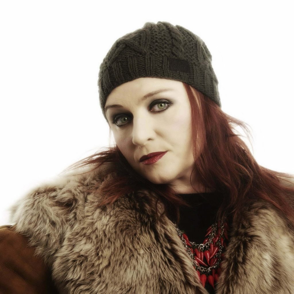 Headshot of Katherine Ellis against a white background. She is wearing a knittted hat and a fur coat.